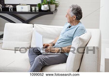 A senior man using a laptop in his living room View Large Photo Image Stock Image - A senior man using a laptop in his living room. Fotosearch
