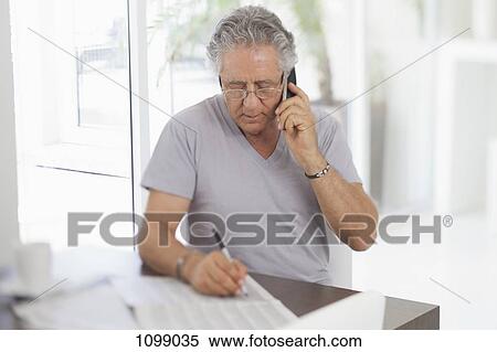 A senior man using the phone and writing on a document View Large Photo Image Stock Photography - A senior man using the phone and writing on a document. Fotosearch