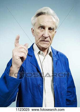 Stock Photography - A senior man wearing coveralls and pointing while talking. Fotosearch