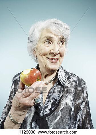 Stock Photo - A senior woman holding an apple with a bite out of it. Fotosearch