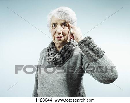 Picture - A serious senior woman pointing to her temple. Fotosearch