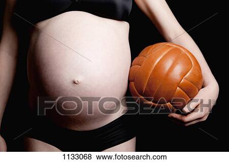 Stock Photo - A shirtless pregnant woman carrying an old fashioned soccer ball, midsection. Fotosearch