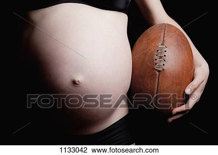 A shirtless pregnant woman holding an old fashioned football, midsection View Large Photo Image Stock Image - A shirtless pregnant woman holding an old fashioned football, midsection. Fotosearch