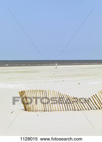 Stock Photography - A slanting fence on a beach and the sea in the background. Fotosearch