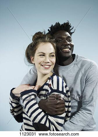 Stock Image - A smiling young man embracing his smiling girlfriend from behind. Fotosearch