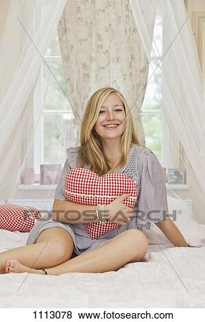 Stock Photo - A teenage girl hugging a heart shaped pillow. Fotosearch