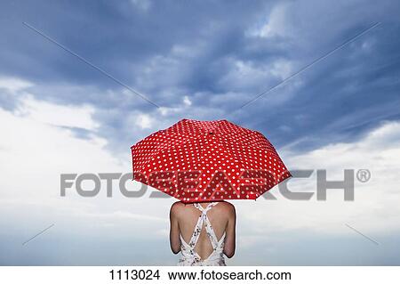 Picture - A woman holding a red polka dot umbrella, rear view. Fotosearch