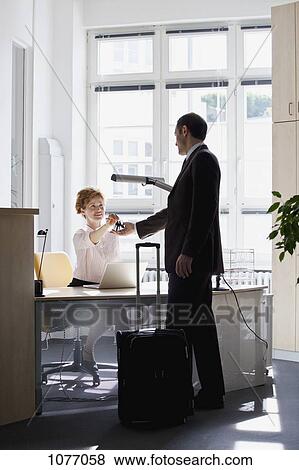 A woman sitting at a desk handing a businessman keys View Large Photo Image Stock Photo - A woman sitting at a desk handing a businessman keys. Fotosearch