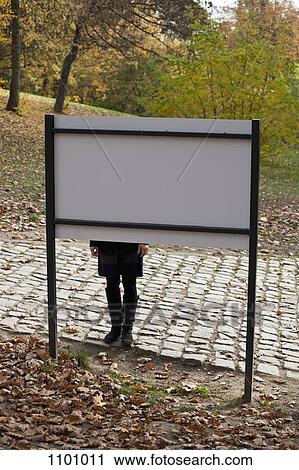 Stock Image - A woman standing behind a sign in a park. Fotosearch