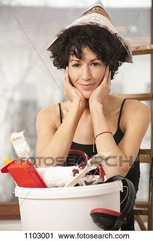 Stock Image - A woman wearing a paper hat leaning on a bucket of paint supplies. Fotosearch