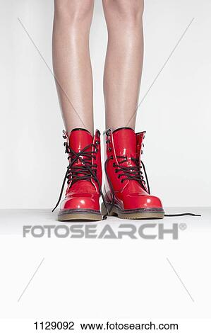 Stock Image - A woman wearing red patent leather boots, low section. Fotosearch