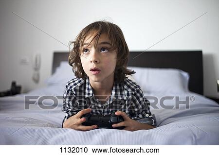 A young boy holding a video game controller looking concentrated View Large Photo Image Stock Image - A young boy holding a video game controller looking concentrated. Fotosearch
