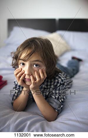 A young boy lying on a bed looking sad View Large Photo Image Stock Image - A young boy lying on a bed looking sad. Fotosearch