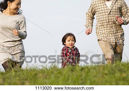 Stock Image - A young boy running in the park in between his mother and father. Fotosearch