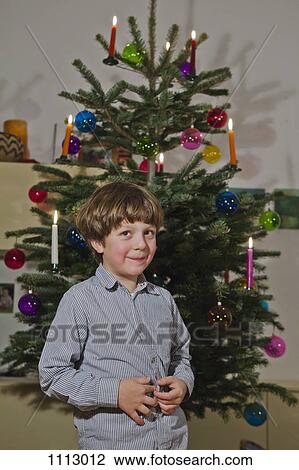 Stock Image - A young boy standing in front of a decorated Christmas tree. Fotosearch