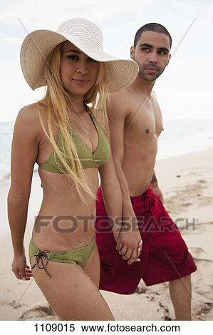 Stock Photography - A young couple holding hands and walking on the beach. Fotosearch