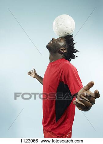 Stock Photograph - A young man balancing a soccer ball on her forehead. Fotosearch