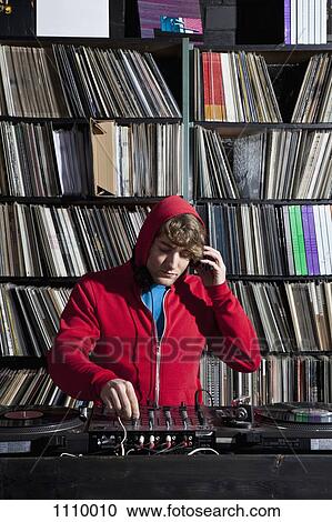Stock Image - A young man using decks and a sound mixer at a record store. Fotosearch