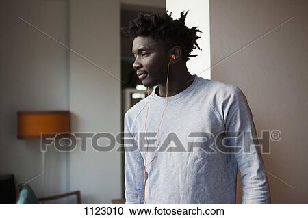 Stock Image - A young man wearing earbuds and looking away. Fotosearch