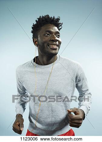 Stock Photograph - A young man wearing earbuds and running, studio shot. Fotosearch