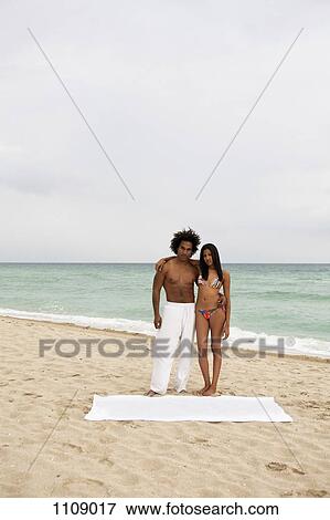 Stock Photo - An attractive young couple standing on a beach. Fotosearch