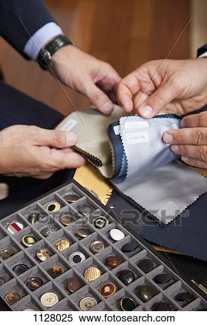 Stock Photography - Detail of a tray of buttons and two men looking at fabric samples. Fotosearch