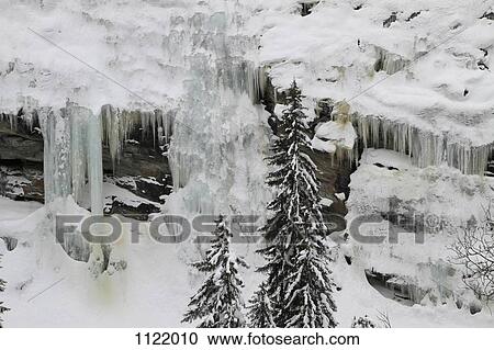 Stock Image - Frozen waterfalls and icicles by mountain side. Fotosearch
