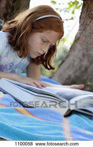 Girl lying down reading book in park View Large Photo Image Stock Photo - Girl lying down reading book in park. Fotosearch
