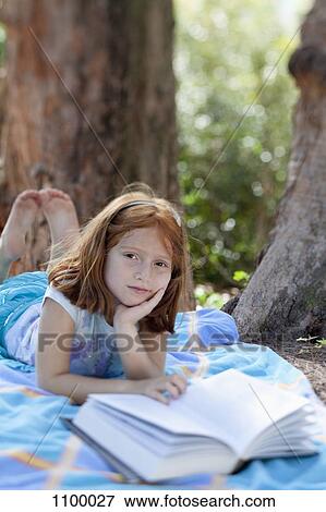 Girl lying on blanket in park with book View Large Photo Image Stock Photo - Girl lying on blanket in park with book. Fotosearch