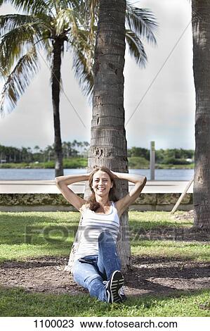 Stock Image - Girl relaxing against palm tree. Fotosearch