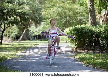 Stock Image - Girl riding bike through park. Fotosearch
