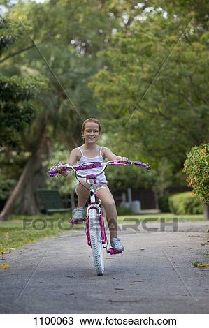 Stock Image - Girl riding bike through park. Fotosearch
