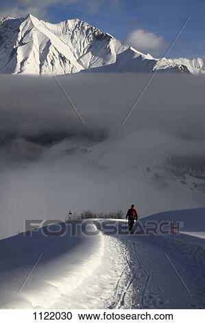Stock Image - Hiker walking snowy footpath with view of mountain range in background. Fotosearch