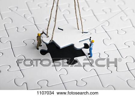 Miniature workmen guiding a hanging puzzle piece into place View Large Photo Image Picture - Miniature workmen guiding a hanging puzzle piece into place. Fotosearch