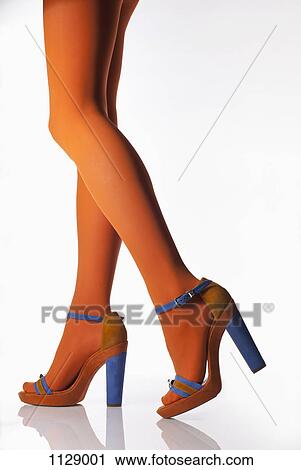 Stock Image - Side view of a woman wearing orange tights and high heels, low section. Fotosearch