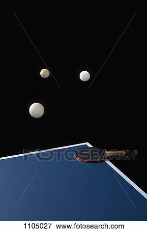 Stock Photo - Table tennis balls mid-air and a bat on a table. Fotosearch