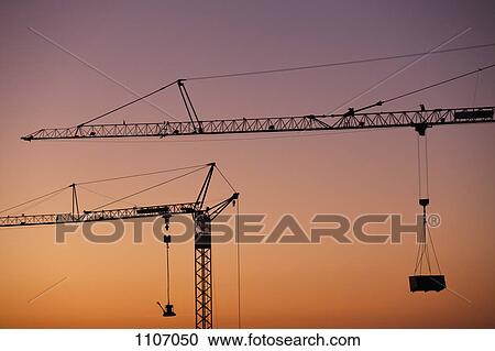 Two construction cranes silhouetted against a sunset sky View Large Photo Image Stock Image - Two construction cranes silhouetted against a sunset sky. Fotosearch