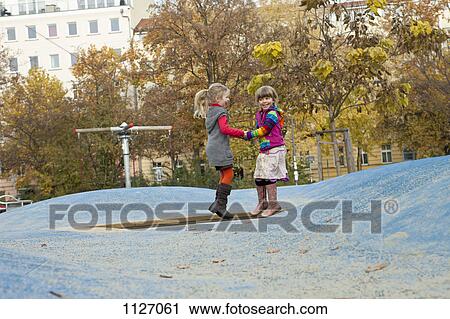 Stock Image - Two girls bounce on small trampoline in park. Fotosearch