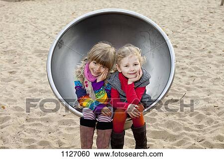 Two girls sitting on spherical metal chair in park View Large Photo Image Stock Image - Two girls sitting on spherical metal chair in park. Fotosearch