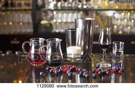 Stock Image - Various glassware with liquids in them next to a cocktail shaker on a bar counter. Fotosearch