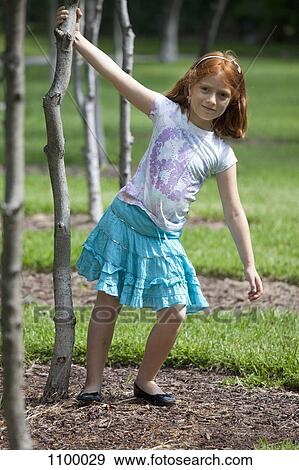 Stock Photo - Young girl in park holding onto tree. Fotosearch