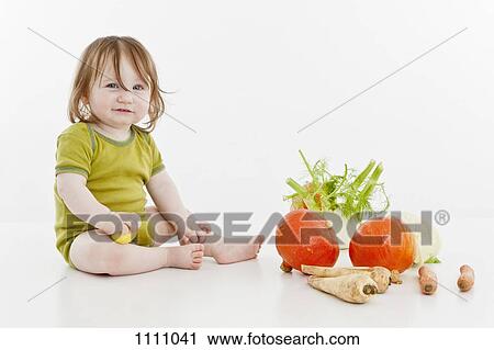 Stock Image - A baby girl sitting with vegetables. Fotosearch