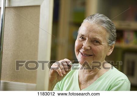 Stock Image - A cheerful senior woman holding a paintbrush. Fotosearch
