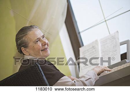 Stock Image - A cheerful senior woman playing an upright piano. Fotosearch