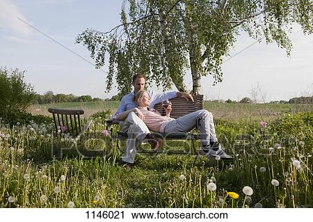 Stock Image - A couple enjoying sunshine and wine on a bench in their backyard. Fotosearch