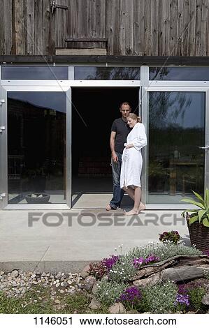 Stock Image - A couple leaning against the doorway of their house in the morning. Fotosearch