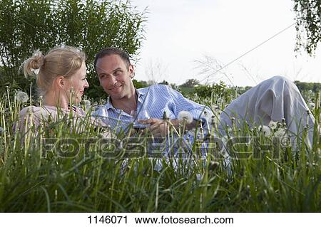 Stock Image - A couple lying in the grass enjoying some red wine. Fotosearch
