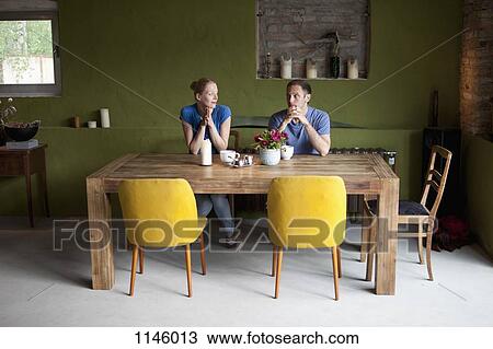 A couple sitting at a dining table looking at each other uncertainly View Large Photo Image Stock Image - A couple sitting at a dining table looking at each other uncertainly. Fotosearch