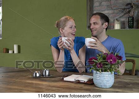 Stock Image - A couple sitting at a dining table with a personal organizer, talking excitedly. Fotosearch