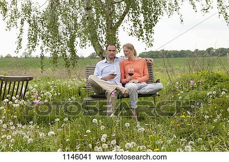 A couple sitting on a bench in their backyard enjoying a glass of red wine View Large Photo Image Stock Image - A couple sitting on a bench in their backyard enjoying a glass of red wine. Fotosearch